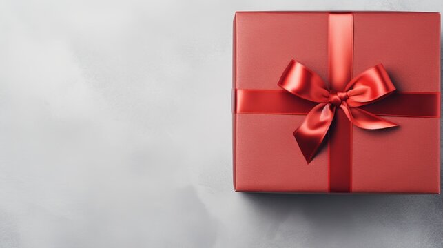 Luxurious red gift box with satin ribbon on a gray background. Elegant present wrapped with a bow. Concept of giving and celebration with a stylish gift.