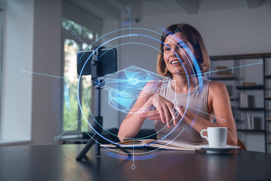 Happy woman is making video blog using smartphone on a tripod explaining with hands at office workplace. Concept of online stream, business education, conference call. Education hologram