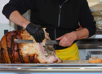 gloved hand of worker  slices roast porchetta with a large sharp knife in a delicatessen