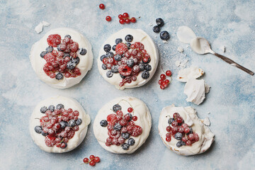 Mini Pavlova meringues with raspberries, red currant and blueberries over light blue concrete...