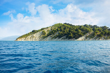 Naklejka premium The sea with a rocky shore on the background of a blue sky with white clouds