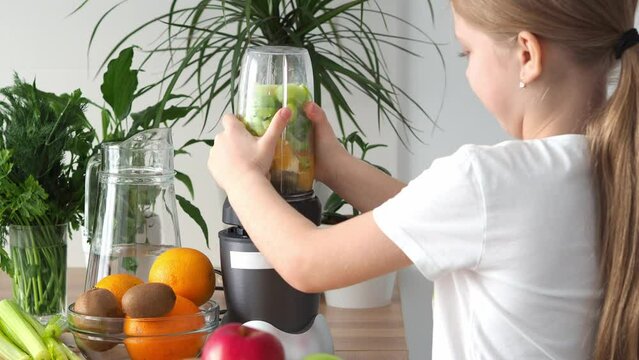 Little girl prepares fresh organic fruit smoothie. Healthy eating concept: close-up of mixing apples, kiwi, orange and bananas in a blender. A child is cooking in the kitchen. Delicious fruit cocktail