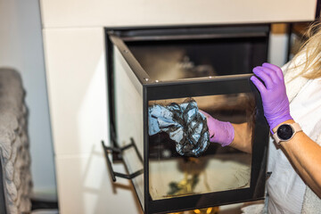 Close-up view of woman cleaning soot from the glass door of the fireplace with paper. Sweden.