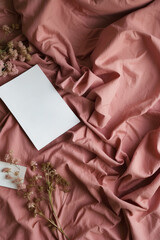 Wrinkled vibrant pink bedding with dry flowers and white paper sheet as a creative copy space. Cozy and warm linen design. Stylish and romantic sleeping concept.