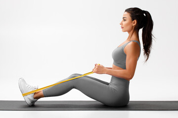 Athletic girl doing resistance band exercise for back on gray background. Fitness woman working out