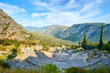 Greek history theme: Athenian Treasury ruins in Delphi against sun, low angle, ultra wide photo, sun and rays, beautiful day. UNESCO World Heritage Site, Greece.