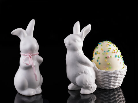 Two decorative white Poezelan Easter bunnies on a black, reflective background