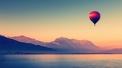 a hot air balloon flying in the sky over a body of water with mountains in the back ground and a body of water in the foreground.