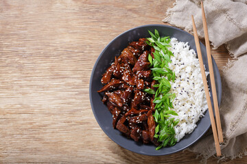 plate of  teriyaki beef, rice, green onion and sesame seeds, top view