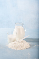 Powdered milk on a blue background with a jug of whole milk