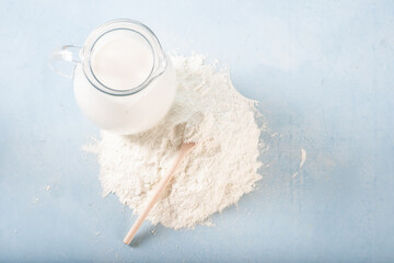 Milk in a glass jug with a pile of wheat flour next to it