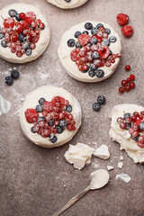 Mini Pavlova meringues with raspberries, red currant and blueberries over gray concrete background. Overhead view, close up