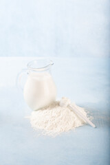 Powdered milk and whole milk in a jug on a light blue background