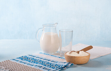 Powdered milk and whole milk in a jug on a light blue background