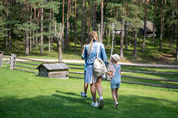 Naklejka na ściany i meble Mother and kids waling on a green grass in a forest setting, with a backdrop of lush pine trees. for themes of motherhood, nature, and simple joys, family bonding and health insurance