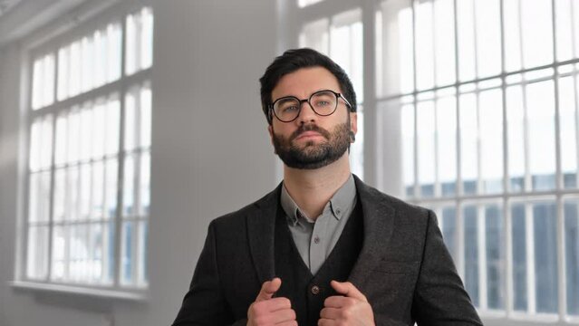 Self-confident and successful man with beard and eyeglasses looking at camera, portrait in building