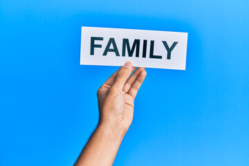 Hand of caucasian man holding paper with family word over isolated blue background