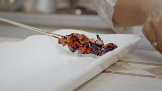 Woman places skewers of chicken satay onto a serviing plate