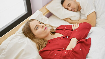 A thoughtful woman and sleeping man portray relationship issues in a bedroom setting, evoking...