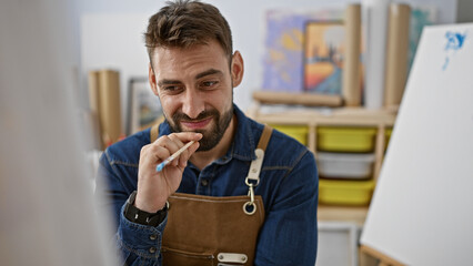 In the heart of the art studio, doubting yet determined, young hispanic man artist in an apron,...