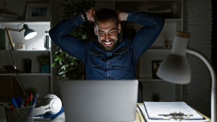 Young hispanic man celebrates laptop work win, boosting office spirits, lighting up the room with...