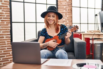 Young caucasian woman musician smiling confident playing ukulele at music studio