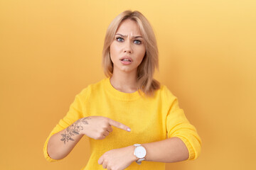 Young caucasian woman wearing yellow sweater in hurry pointing to watch time, impatience, upset and...
