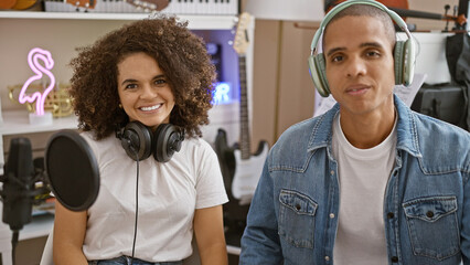 Confident musicians smiling, listening to melody through headphones in music studio, happy artists...