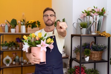 Middle age man with beard working at florist shop holding plant pointing with finger to the camera and to you, confident gesture looking serious