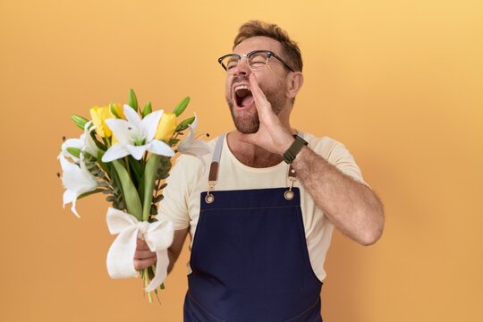 Middle age man with beard florist shop holding flowers shouting and screaming loud to side with hand on mouth. communication concept.