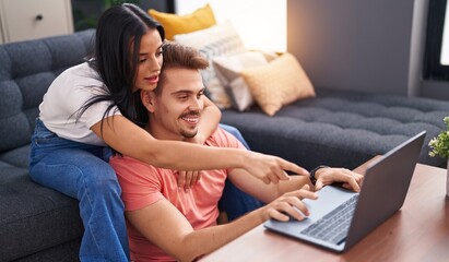Man and woman couple using laptop sitting on sofa at home