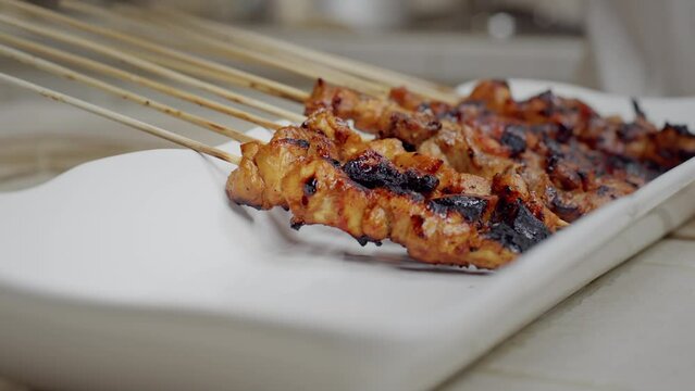 Woman places skewers of chicken satay onto a serviing plate