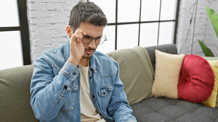 Handsome hispanic man adjusting glasses in a stylish living room