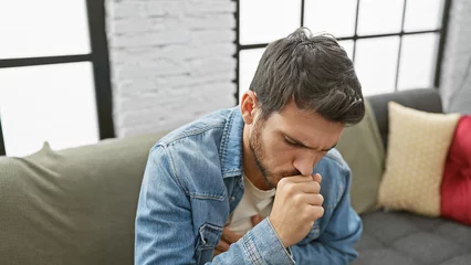 Fotobehang Hispanic man coughing in a modern living room, portraying illness © Krakenimages.com