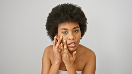 A thoughtful african american woman with curly hair poses against a white background, touching her...