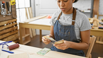 African woman counting south african rands in a carpentry studio.