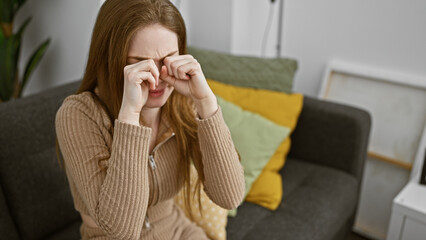 A stressed young woman rubbing her eyes at home, showing signs of fatigue or headache.