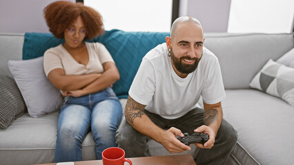 Upset beautiful couple sitting together at home, boyfriend engrossed in video game play leaves...