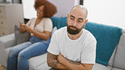 Beautiful couple looking upset while sitting together at home, girlfriend engrossed in smartphone...