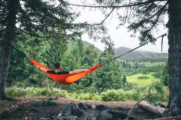 man in hammock at camping site mountains on background