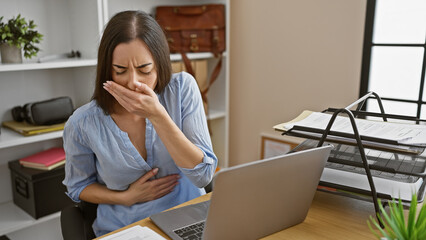Beautiful young hispanic woman struggling with stomach ache while working on laptop at office desk