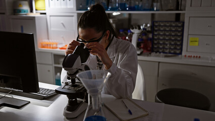 Immersed in discovery, beautiful young hispanic female scientist working late night at lab,...