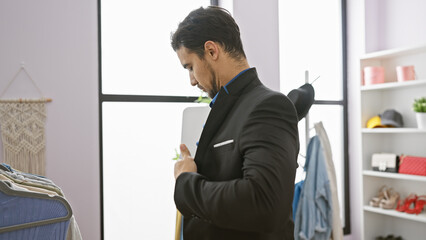 Handsome hispanic man adjusting suit in modern dressing room with clothing rack and mirror.