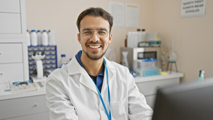 Handsome young hispanic man with beard smiling in laboratory wearing lab coat and glasses