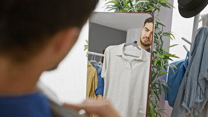A handsome young hispanic man in a clothing room, contemplating a shirt while looking in the mirror...