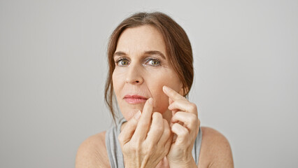 A middle-aged woman carefully examines her skin against a white background, embodying themes of...