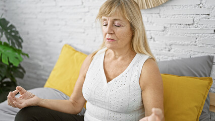 Fototapeta premium Awake and focused, middle age blonde woman enjoys morning yoga exercise sitting on bed, embracing calm and balance in her bedroom