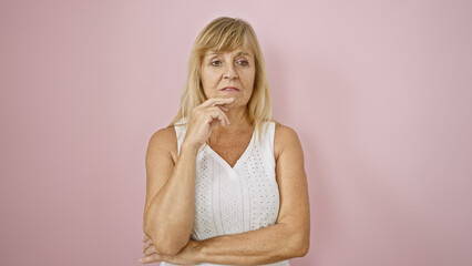 Middle age beautiful blonde woman wears serious expression, standing confidently over isolated pink...