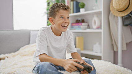 Adorable blond boy, happily engrossed in gaming, comfortably sitting on sofa at home, confidently using gaming device, radiating pure joy. - obrazy, fototapety, plakaty