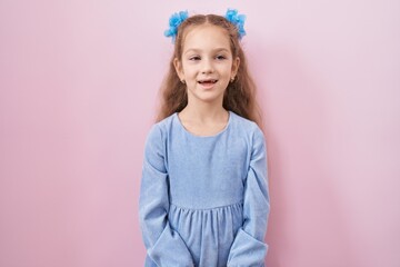 Young little girl standing over pink background looking positive and happy standing and smiling with a confident smile showing teeth
